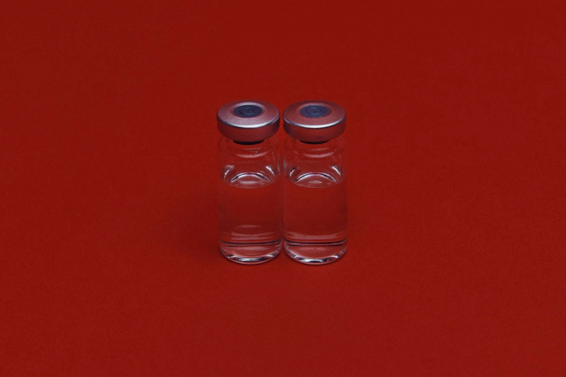 Two glass vials on a red background