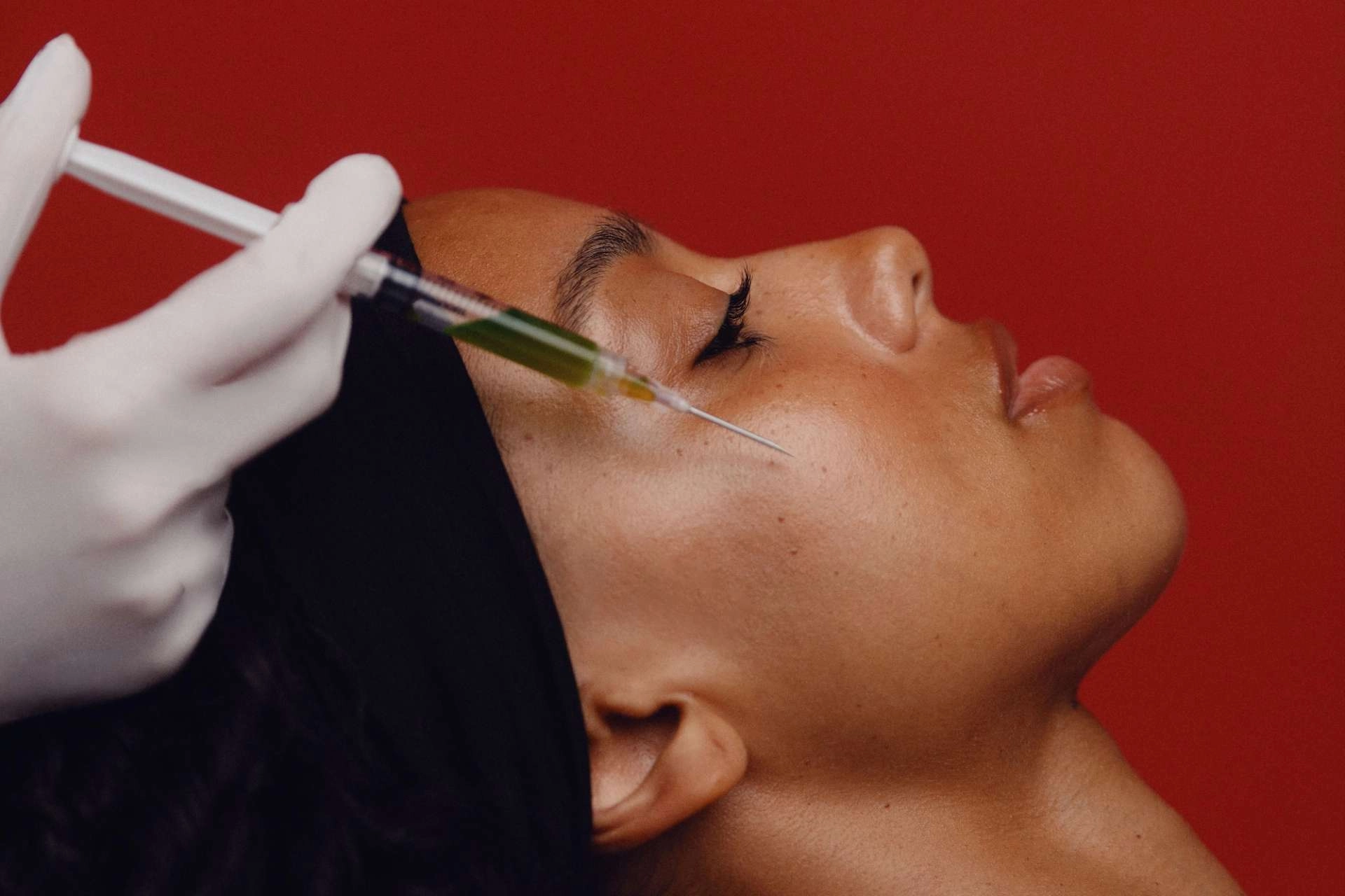 Provider applying a treatment to a client's face against a red wall