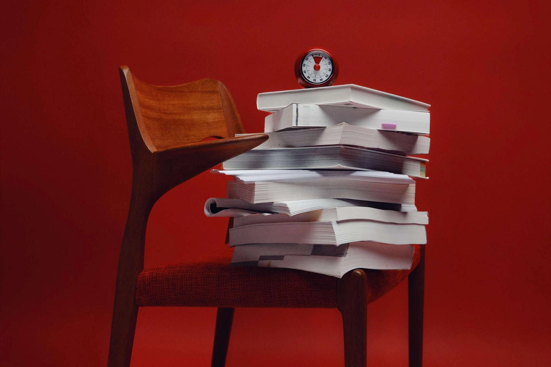 Stack of books on a wooden chair against a red wall