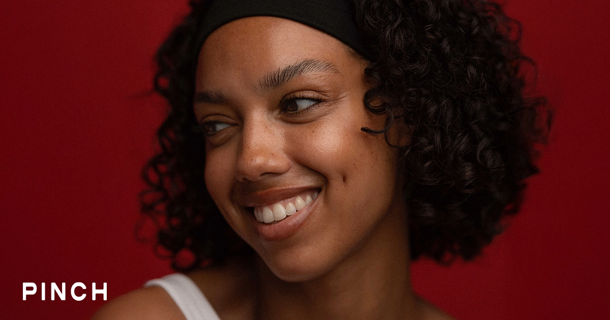 Smiling woman in a Pinch headband against a red background